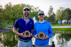 Photo of Illinois State Two Person Scramble winners Dusty Drenth and Michael Fastert holding their championship plaques in front of the fountain at White Pines on APril 26.